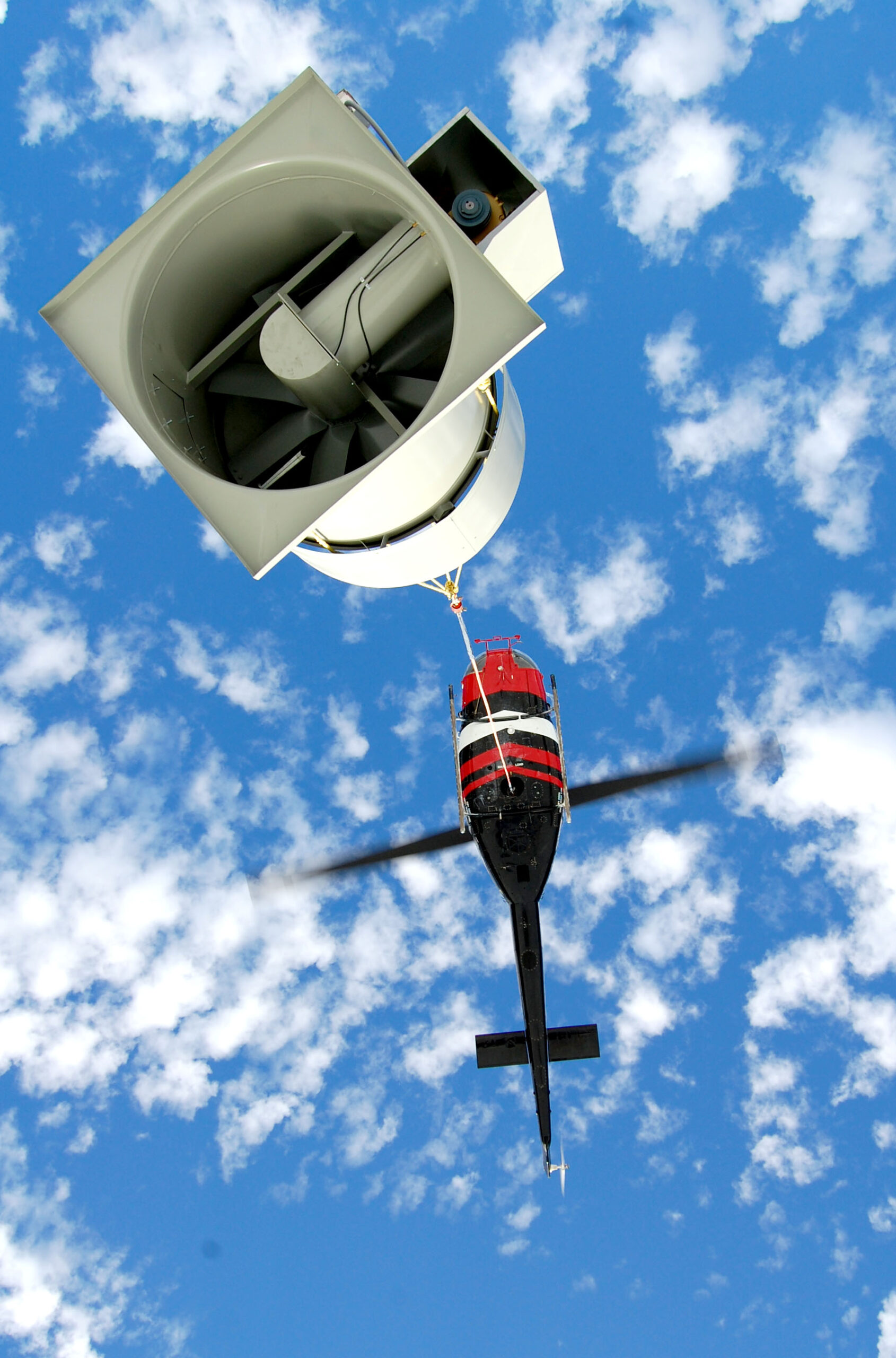 Helicopter carrying exhaust fan from overhead